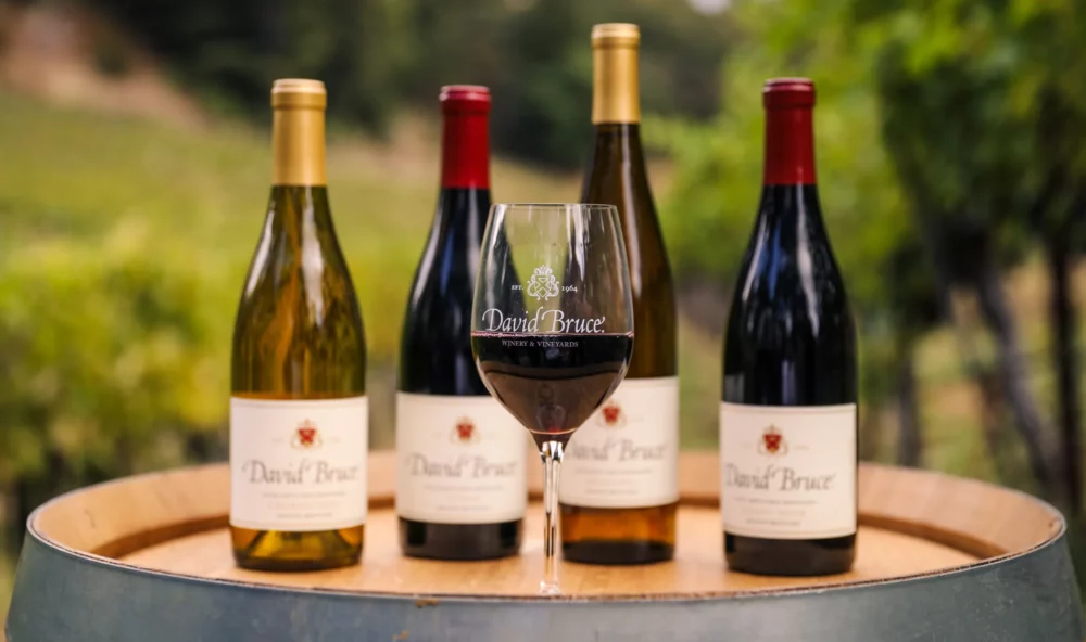 Glass of David Bruce wine on a barrel with a lineup of wine bottles behind